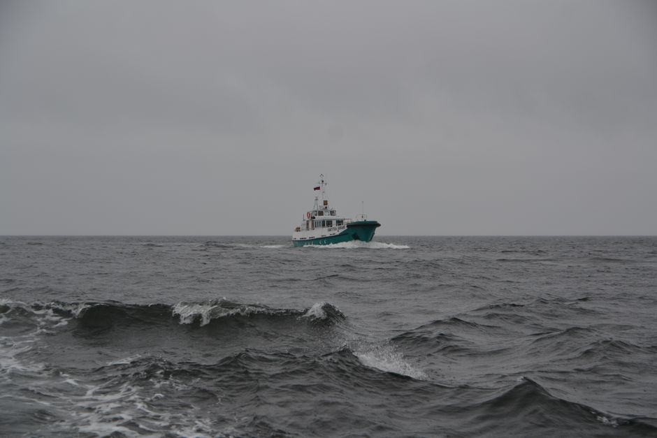 Un barco de pesca navega a través de olas agitadas del océano bajo un cielo nublado, mostrando el transporte marítimo.