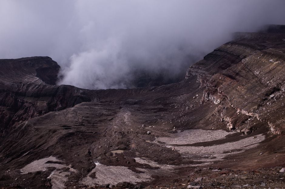 Crater volcánica brumosa mostrada en una densa niebla, capturando un terreno rugoso y dramático.