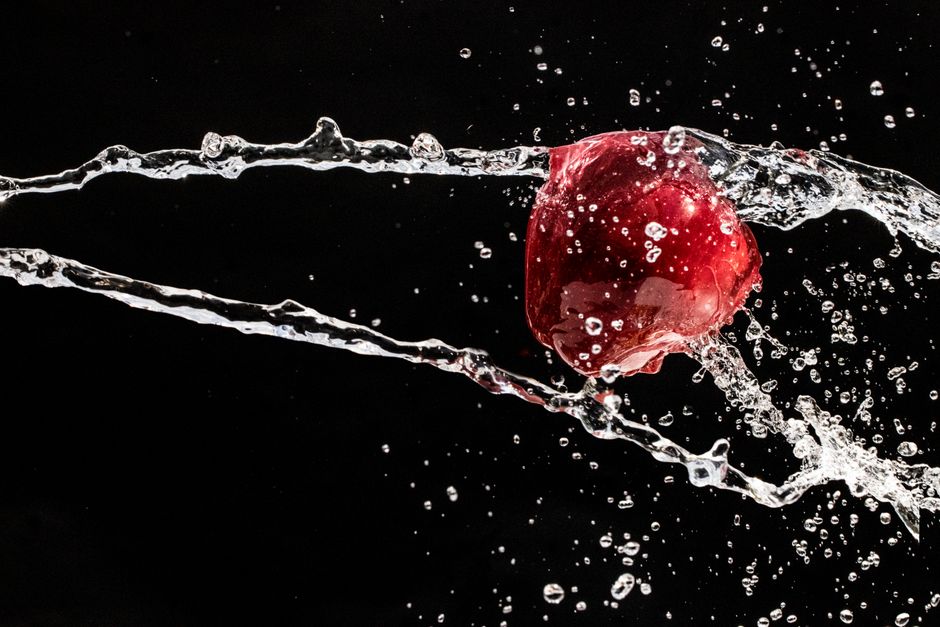 Una vibrante manzana roja atrapada en el aire con salpicaduras dinámicas de agua sobre un fondo negro.