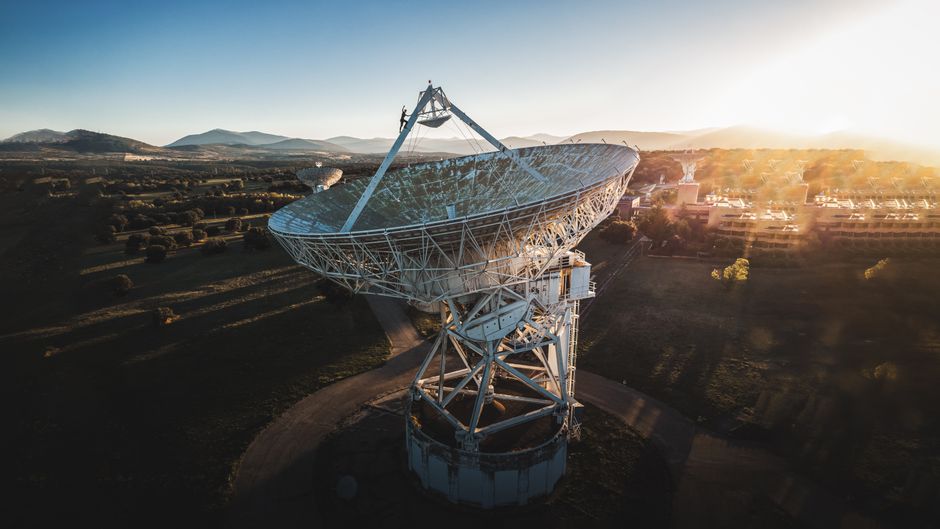 Toma aérea de una gran antena parabólica en un paisaje rural durante el amanecer, mostrando tecnología y naturaleza.