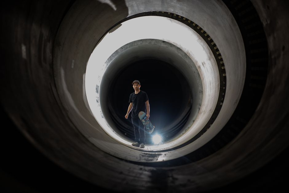 Un skater posa de manera dramática en un túnel oscuro con efecto de luz, creando una imagen impactante.