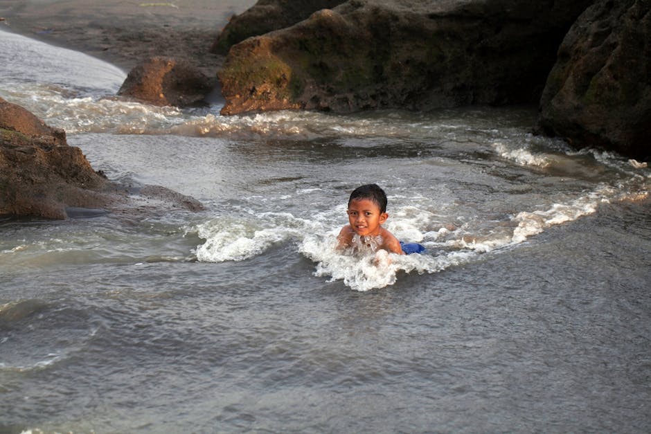 Niño pequeño sonriendo mientras nada entre formaciones rocosas en un arroyo natural.