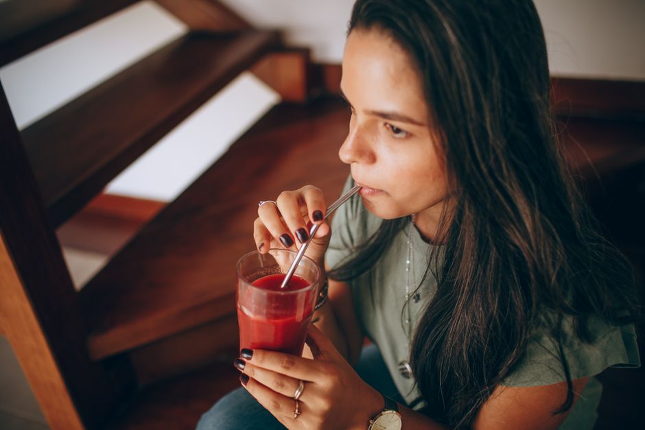 Mujer relajándose en interiores con un refrescante jugo de frutas rojas, disfrutando de su tiempo libre.