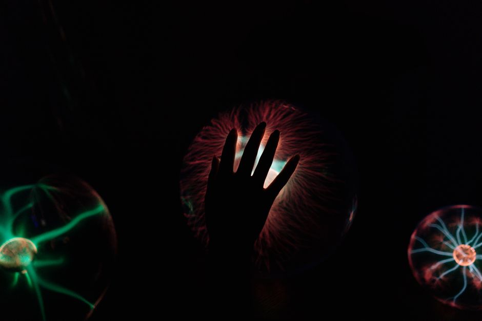Silueta de una mano interactuando con una bola de plasma brillante, ilustrando ondas eléctricas.