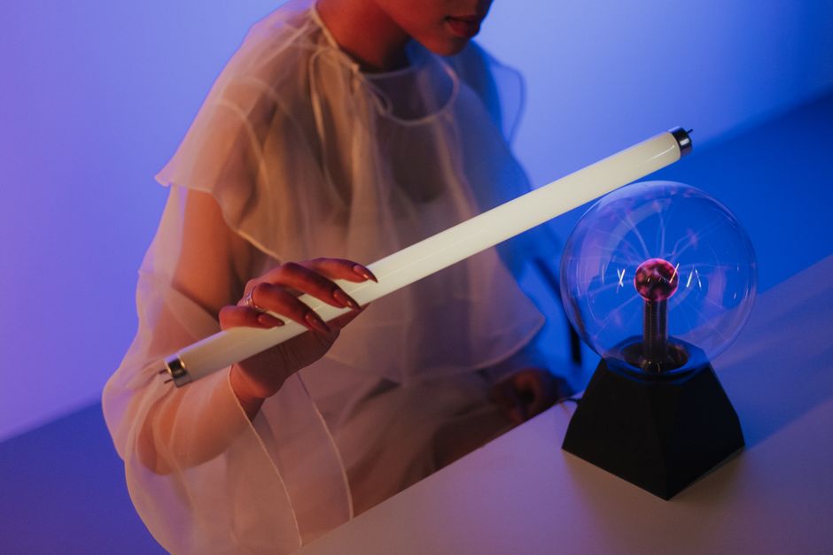 Una mujer sosteniendo una luz de neón cerca de una bola de plasma, demostrando conceptos de electricidad y ciencia.
