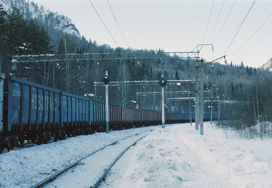 Un tren de carga viaja a través de un paisaje nevado con montañas y árboles en invierno.