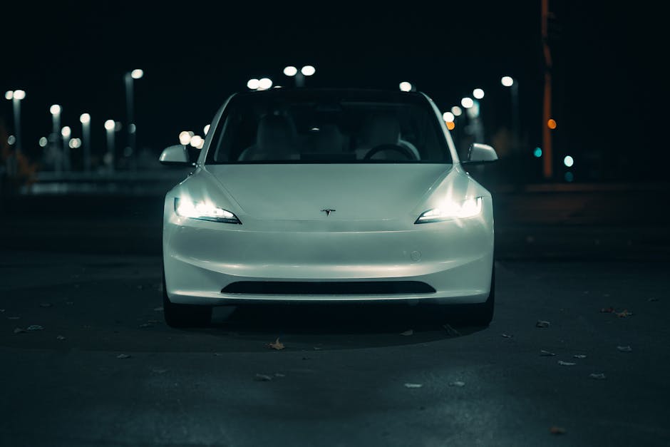 Coche eléctrico blanco capturado de noche con faros brillantes, creando una sensación urbana melancólica.