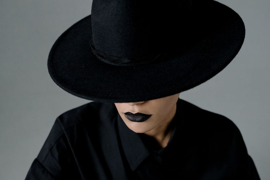 Retrato de una mujer con un sombrero negro de ala ancha, usando lápiz labial negro, creando una vibra misteriosa.