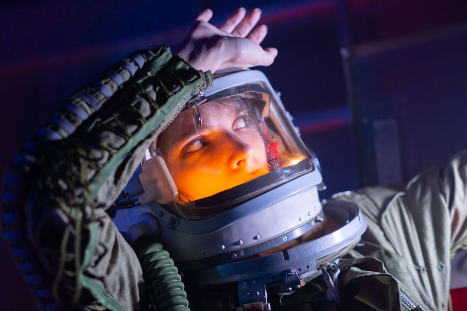 Astronauta femenina en un traje espacial mira hacia arriba, iluminada en un entorno futurista.