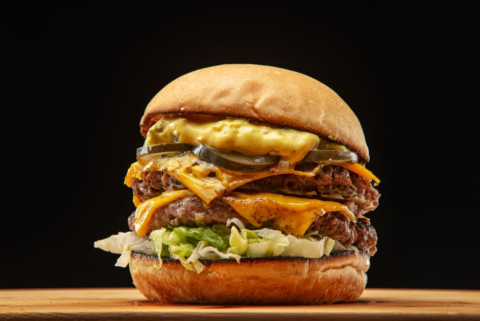 Jugosa hamburguesa con queso, pepinillos, lechuga y salsa, perfecta para amantes de la comida.