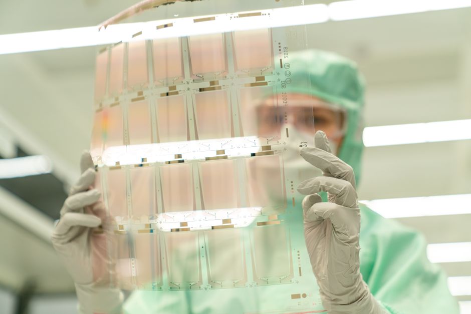 Científica con equipo de protección sosteniendo una hoja de prueba transparente en un laboratorio.