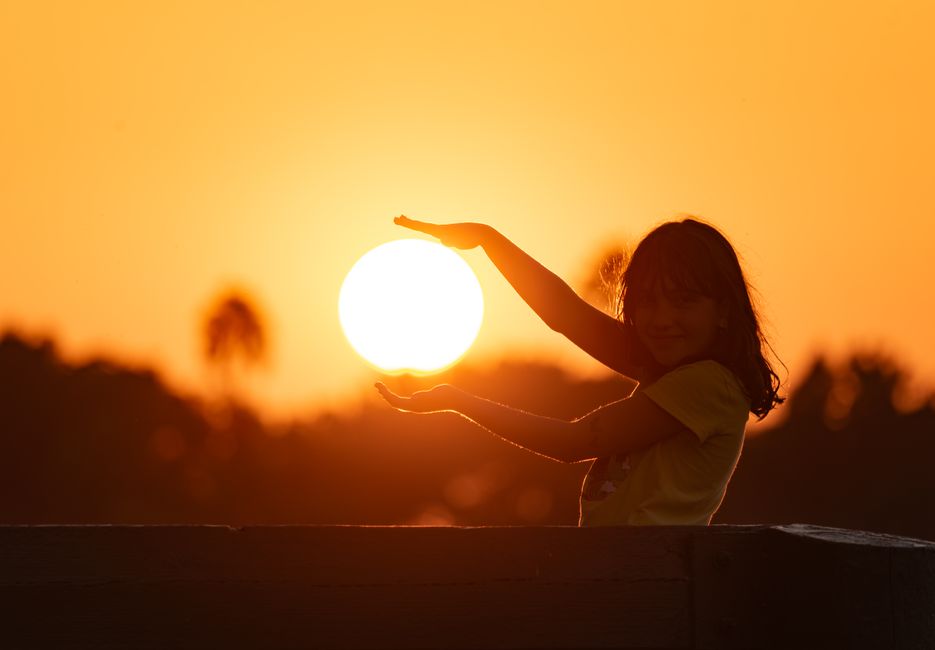 Una niña joven enmarcando juguetonamente el sol durante un vibrante atardecer naranja en Irwindale, CA.