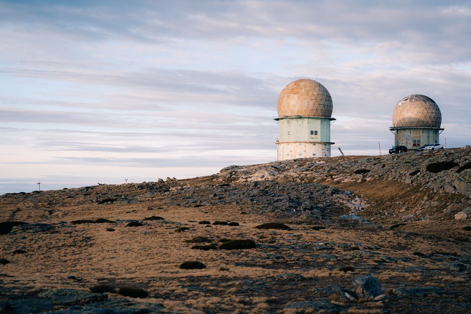 Dos cúpulas de radar en un paisaje rocoso bajo un cielo crepuscular nublado, simbolizando tecnología y aislamiento.