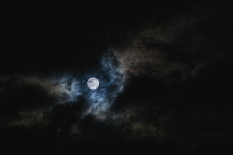 Un fascinante cielo nocturno con la luna llena rodeada de nubes dramáticas, creando una escena misteriosa.