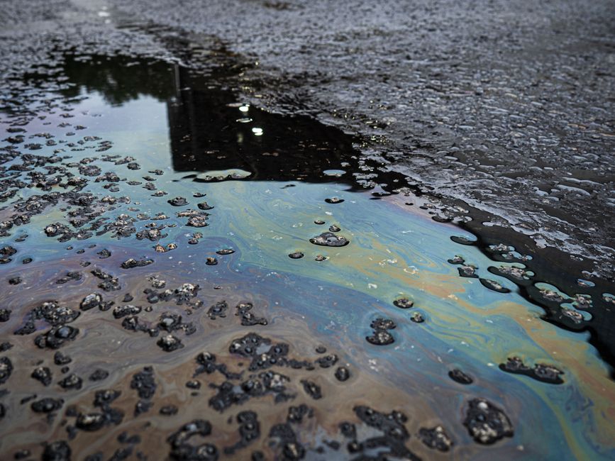 Un vívido derrame de petróleo iridiscente sobre una superficie de asfalto rugosa, que pone de manifiesto la contaminación ambiental.