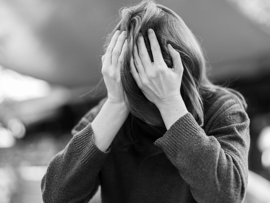 Una mujer en angustia sosteniendo su cabeza entre las manos, capturada en un retrato dramático en blanco y negro.