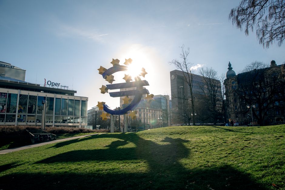 Escultura del Euro en Frankfurt, Alemania, con edificios de paisajes urbanos y luz solar.