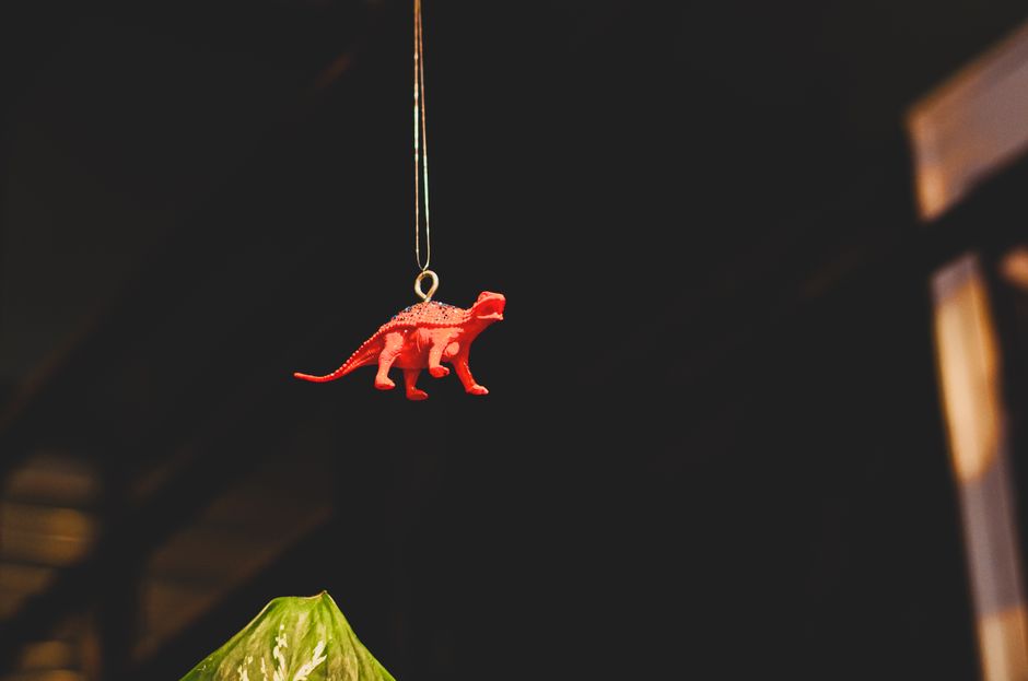 Una figurita de dinosaurio roja colgando de un hilo con espacio oscuro para texto, ideal para proyectos creativos.