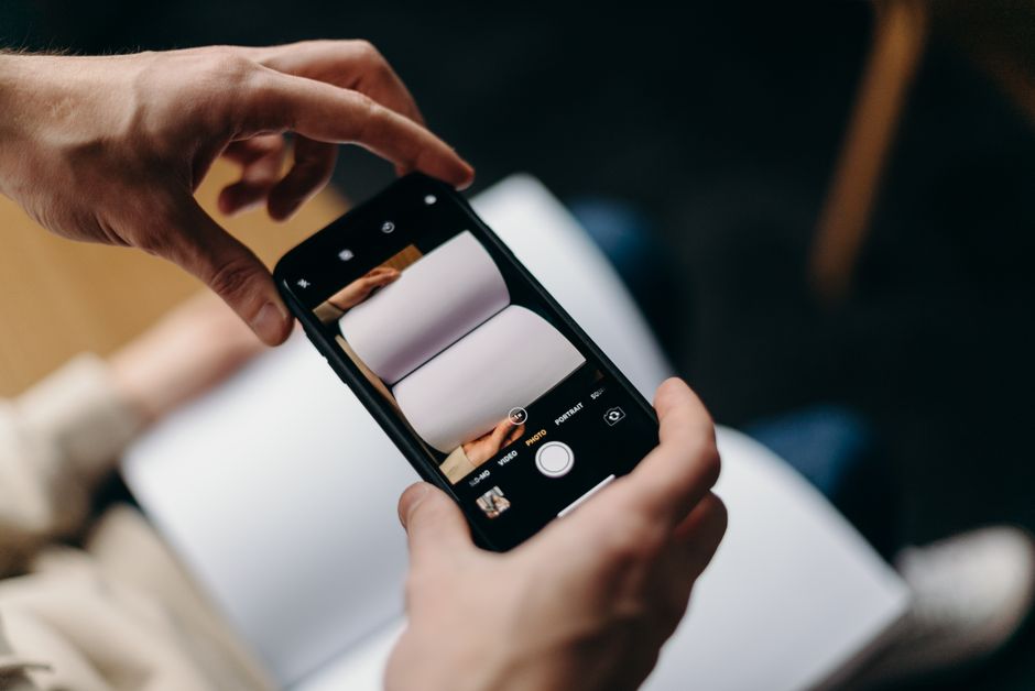 Persona usando un smartphone para fotografiar un libro en blanco abierto. Concepto de fotografía móvil y creatividad.