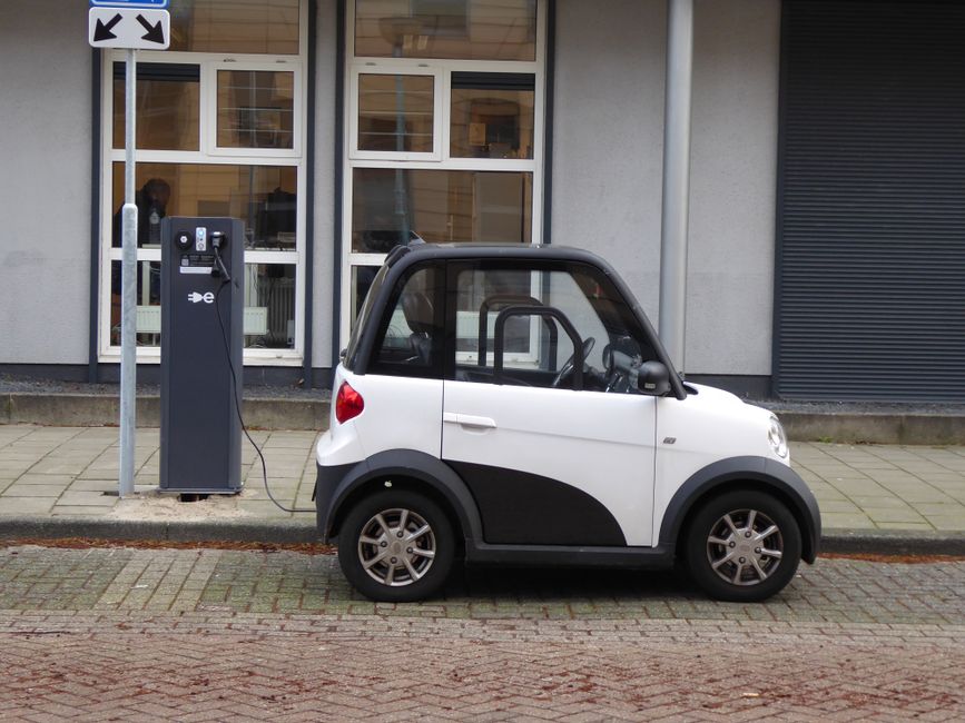 Un coche eléctrico compacto en blanco y negro cargándose en una estación de energía pública.