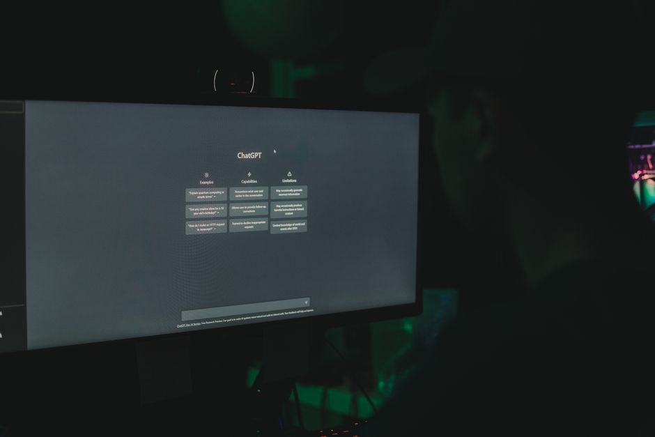 Una persona interactuando con la interfaz de ChatGPT en la pantalla de un ordenador en una habitación poco iluminada.