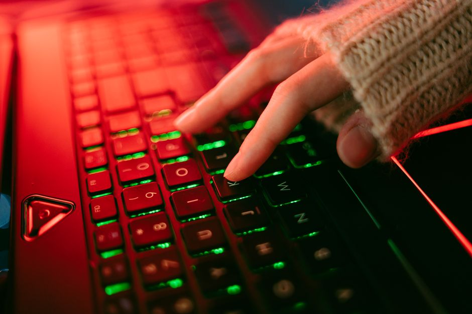 Una mano escribiendo en un teclado retroiluminado en una atmósfera oscura, destacando la iluminación vibrante de las teclas.