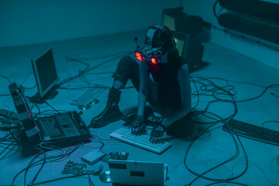 Una mujer con equipo de VR rodeada de computadoras y cables, inmersa en una simulación virtual.
