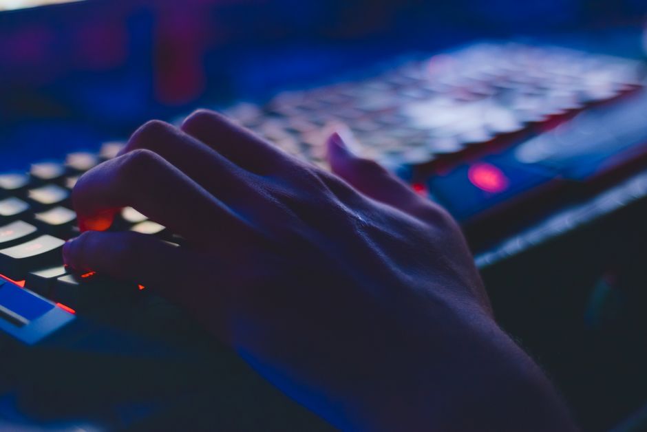 Una mano escribiendo en un teclado brillante con iluminación tenue, perfecta para temas tecnológicos.