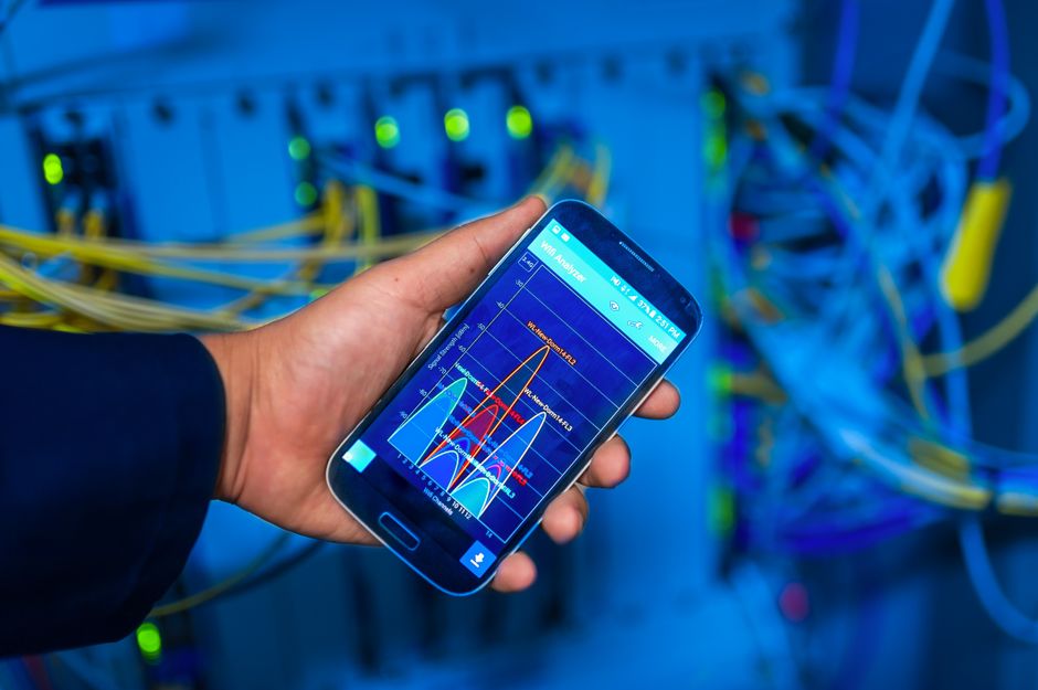 Mano sosteniendo un smartphone que muestra análisis de red en un entorno de servidor de alta tecnología.
