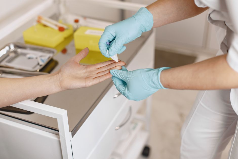 Primer plano de un trabajador de la salud usando guantes para aplicar un vendaje en el dedo de un paciente en un entorno médico.
