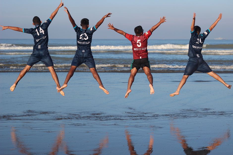 Grupo de adolescentes saltando alegremente en la playa, disfrutando del día soleado juntos.