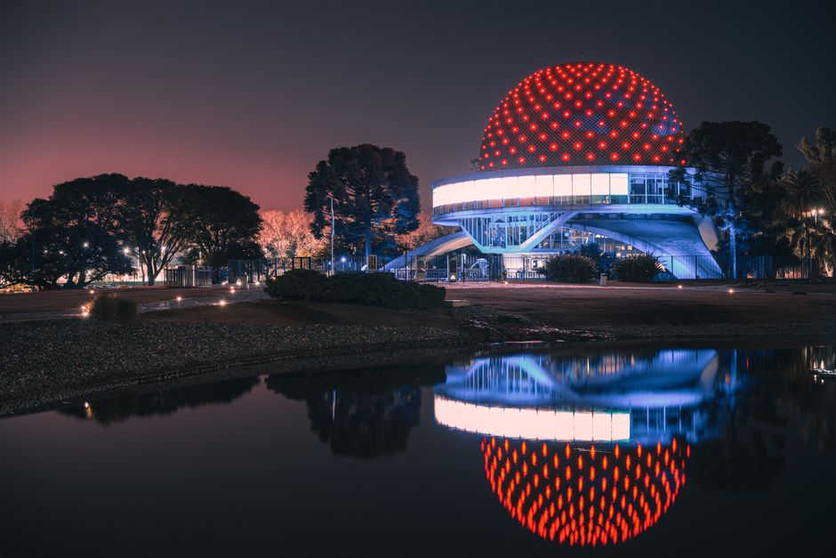 Planetario iluminado de Buenos Aires reflejado en el agua por la noche.