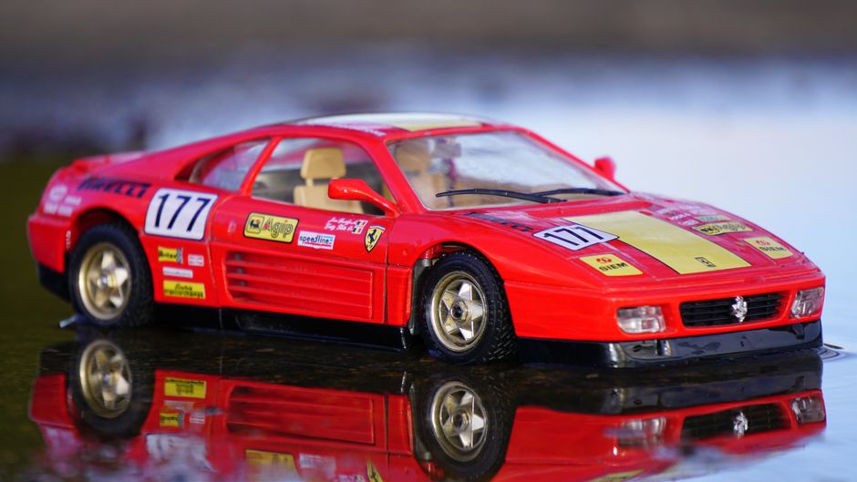 Primer plano de un modelo de coche Ferrari rojo con reflexión en una superficie acuosa.
