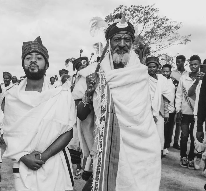 Fotografía en blanco y negro que muestra una procesión tradicional africana con hombres ataviados con vestimenta ceremonial.