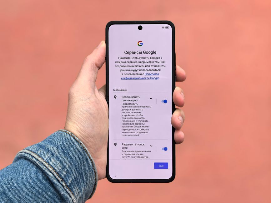 Una persona sostiene un teléfono inteligente que muestra la configuración de Google sobre un fondo simple.