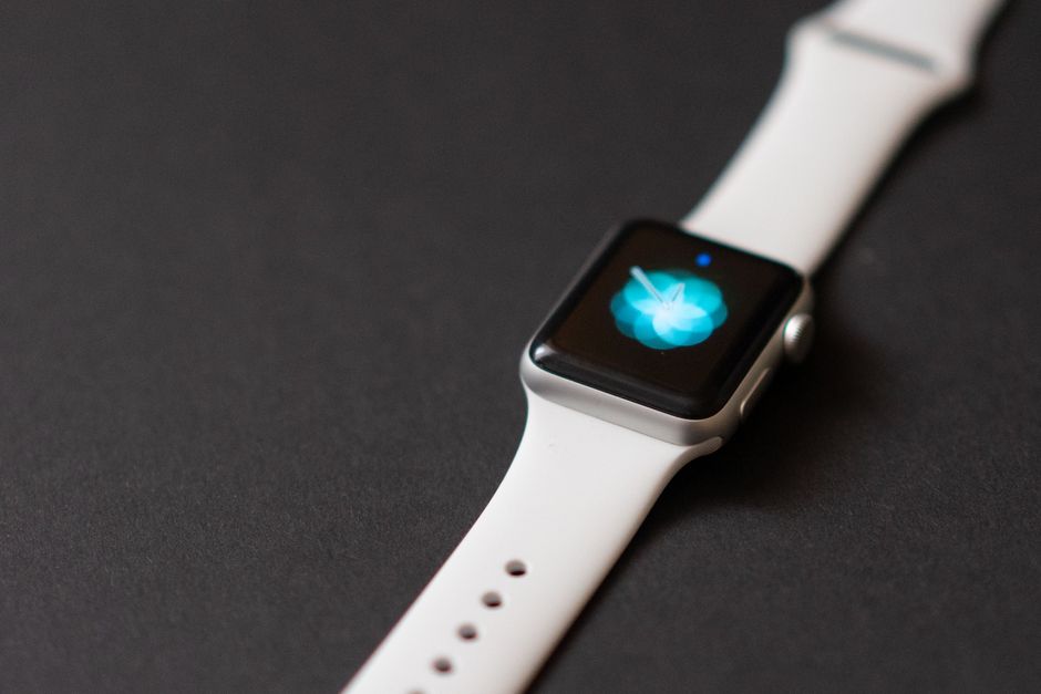 Primer plano de un reloj inteligente elegante con correa blanca sobre una superficie oscura, mostrando su pantalla digital.