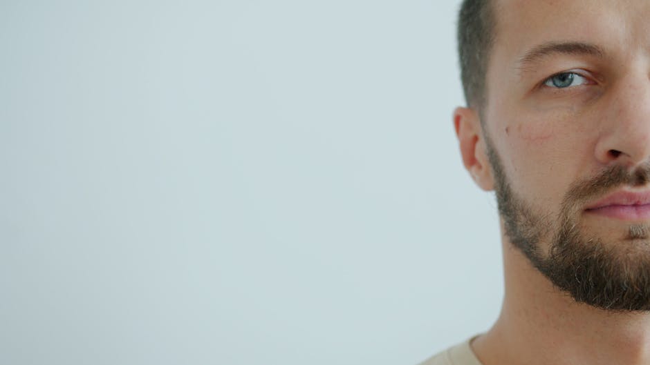 Primer plano minimalista de un hombre con ojos azules y barba sobre un fondo claro.