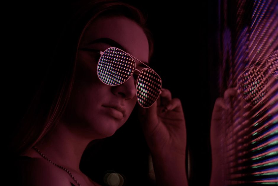 Joven elegante posando en interiores con gafas de sol reflectantes vibrantes, creando un look moderno y atrevido.