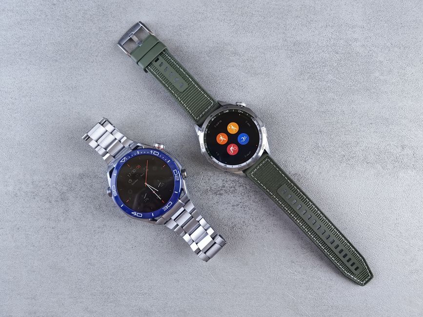 Primer plano de dos relojes inteligentes con correas metálicas y verdes sobre un fondo de hormigón texturizado.