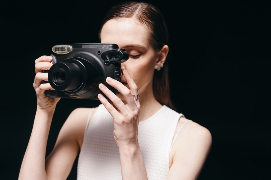 Mujer con estilo usando una cámara instantánea frente a un fondo oscuro, mostrando fotografía moderna.