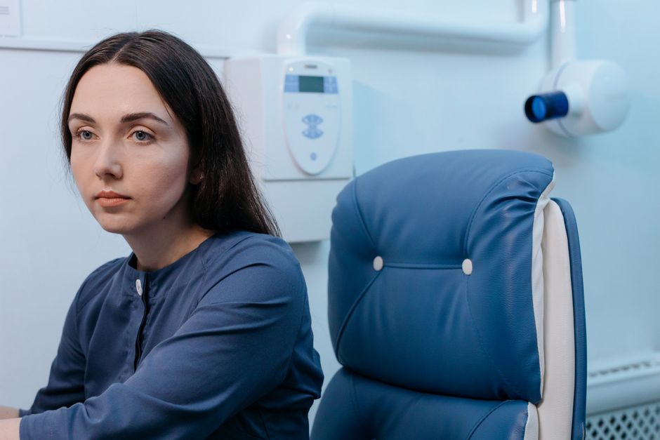 Una mujer reflexiva sentada en una silla azul, ambientada en un entorno de clínica médica.