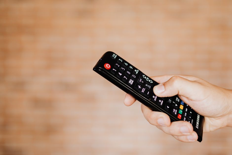 Toma en primer plano de una mano sosteniendo un control remoto de TV contra un fondo borroso.