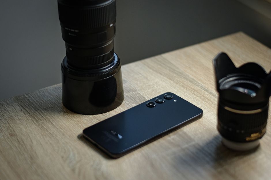 Un smartphone elegante colocado junto a lentes de cámara en un escritorio de madera, capturando tecnología y fotografía.