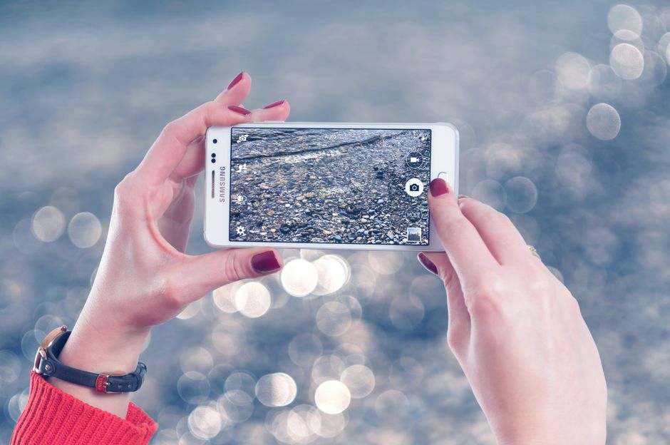 Manos de una mujer tomando una fotografía de piedras junto al agua con un smartphone.