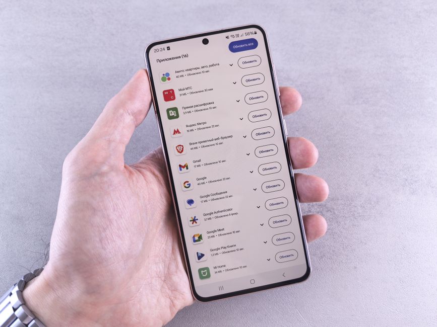 Primer plano de una mano sosteniendo un smartphone que muestra actualizaciones de aplicaciones sobre un fondo claro.