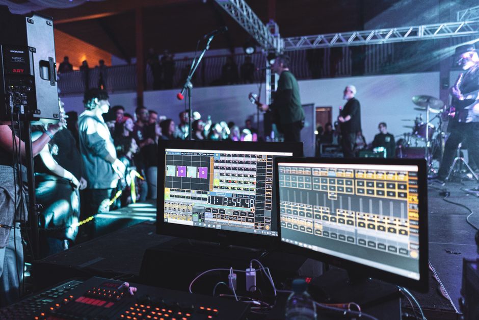 Escena de concierto en vivo con configuración de ingeniería de sonido y banda en el escenario.