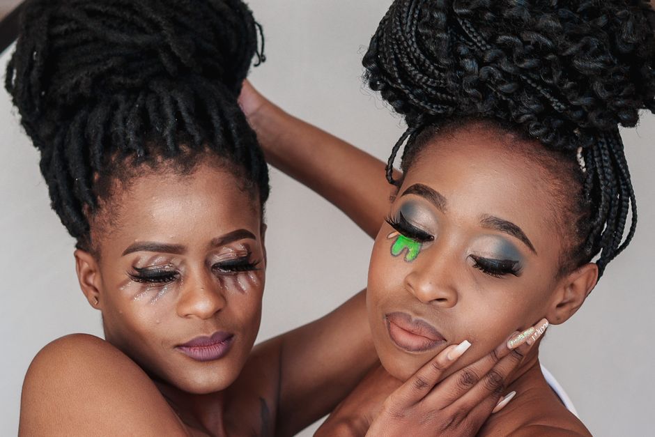 Retrato en primer plano de dos mujeres que muestran elegantes peinados trenzados y maquillaje creativo.