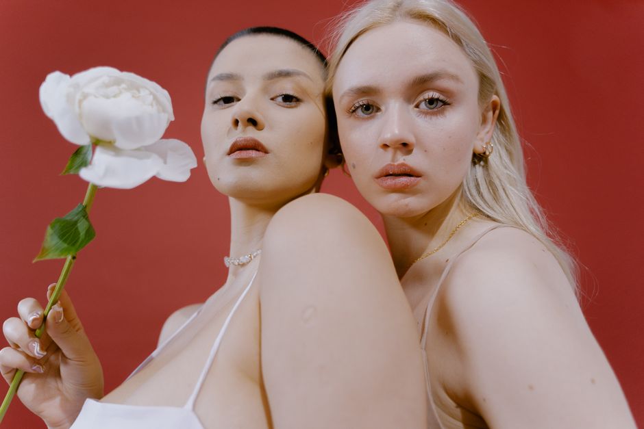 Dos mujeres posan con una peonía blanca frente a un fondo rojo vibrante, exudando elegancia y estilo.