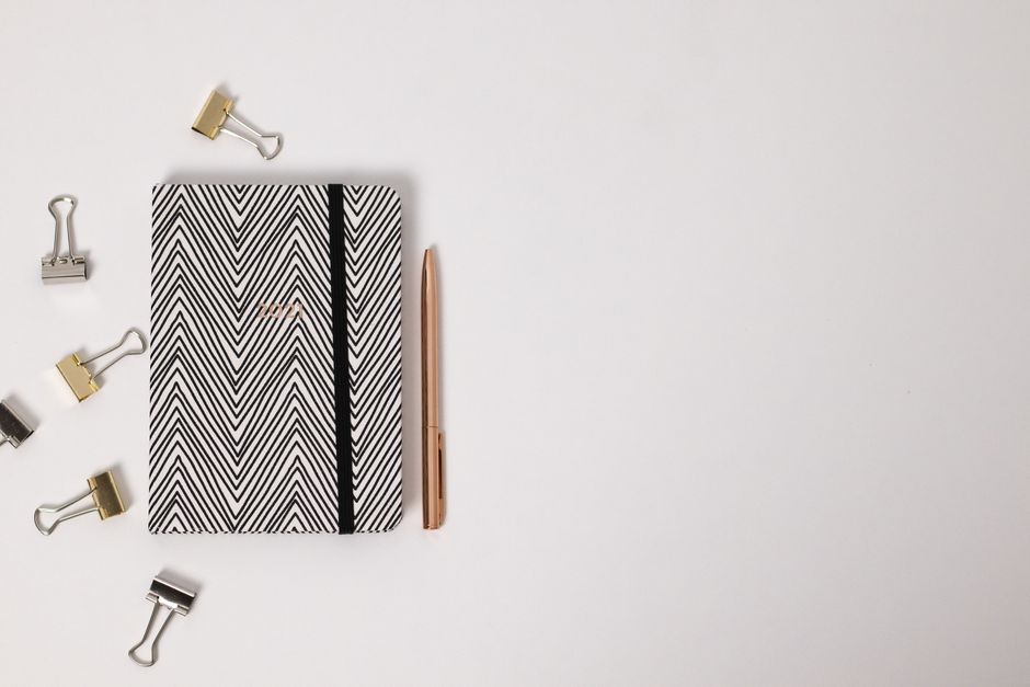 Un planificador en blanco y negro con clips de encuadernación y un bolígrafo, que ofrece amplio espacio para escribir.