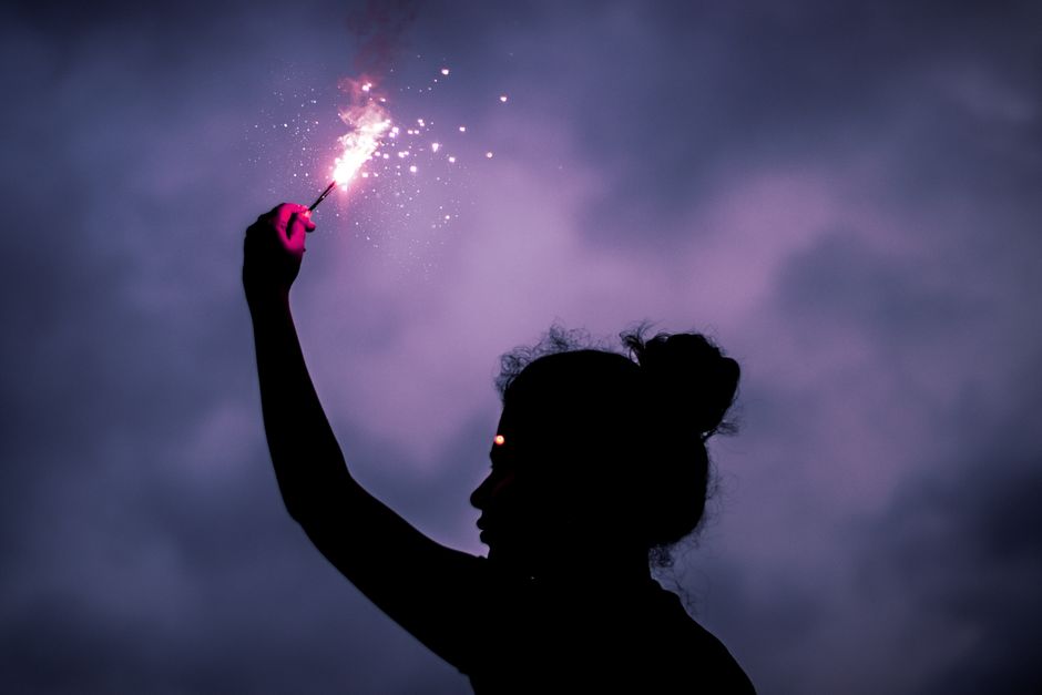 Silueta de una mujer con una bengala brillante contra un cielo nublado y oscuro.